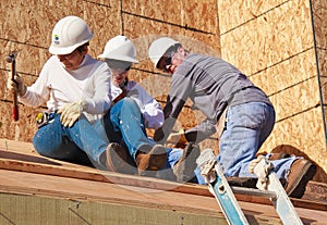 Three people build roof for home for Habitat For Humanity