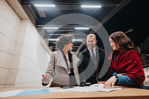 Three people examine documents during an outdoor evening meeting, showcasing teamwork and planning in an urban setting.