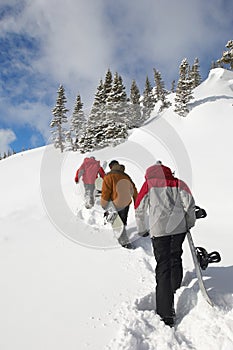 Three People With Snowboards Hiking Up Snow