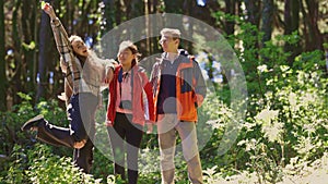 Three people are standing in a forest, one of them wearing a red jacket