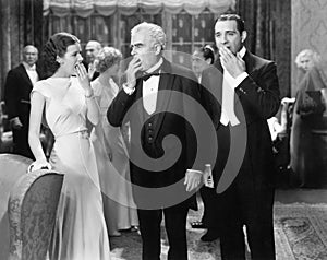 Three people standing together at a formal party yawning and being bored