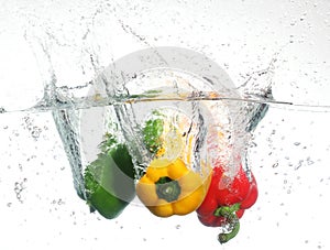 Three peppers falling into water, over white