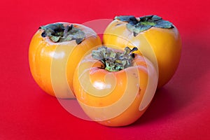 Three persimmons on red background
