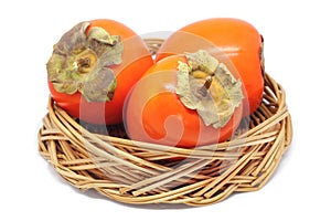 Three Persimmons In a Wicker Bowl Isolated On White