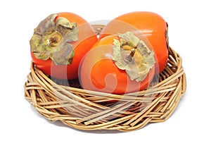 Three Persimmons In a Wicker Bowl Isolated On White photo