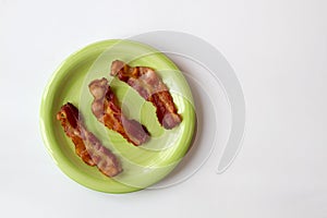 Three Pieces of Bacon on a Green Plate isolated on a White Background