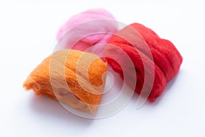 Three pieces of orange, pink and red wool on white background. Concept of felting creative hobby. Selective focus.