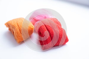 Three pieces of orange, pink and red wool on white background. Concept of felting creative hobby. Selective focus.