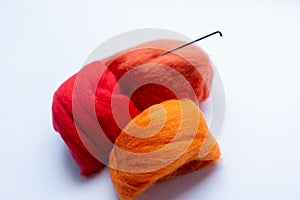 Three pieces of orange and red wool with sticked needle on white background. Concept of felting creative hobby. Selective focus.