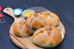 Three pieces of Pan de muerto on wooden board on dark background. Copy space