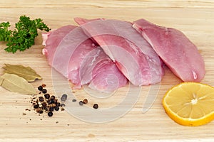 Three pieces of raw turkey steak with spices on a wooden board