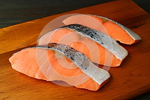 Three pieces of sliced fresh raw salmons on a wooden cutting board
