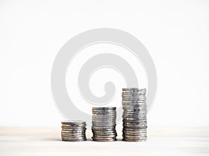 Three piles of silver coin stack arranged as a graph step on wood desk and white background.