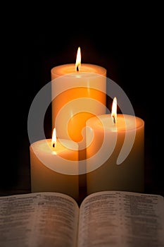 Three Pillar Candles Burning in a Dark Room with a Bible