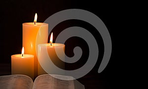 Three Pillar Candles Burning in a Dark Room with a Bible