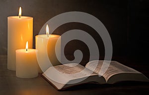 Three Pillar Candles Burning in a Dark Room with a Bible