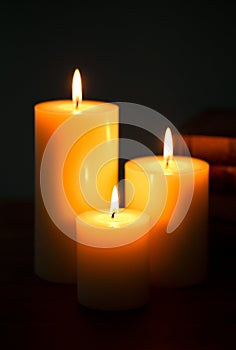 Three Pillar Candles Burning in a Dark Room with a Stack of Antique Books