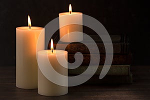 Three Pillar Candles Burning in a Dark Room with a Stack of Antique Books
