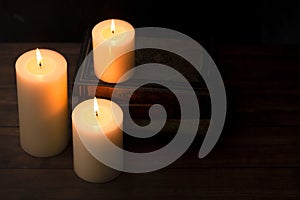 Three Pillar Candles Burning in a Dark Room with a Stack of Antique Books