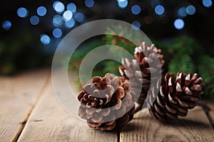 Three pine cones and fir tree branch on rustic wooden table. Christmas greeting card with bokeh.