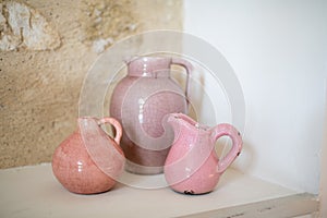 Three pink ceramic pitchers with a stone wall