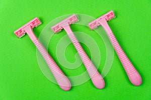 Three pink disposable razors on a green . Personal hygiene items for shaving