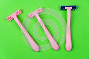 Three pink disposable razors on a green . Personal hygiene items for shaving