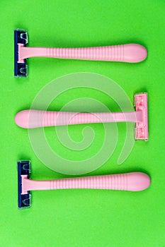 Three pink disposable razors on a green . Personal hygiene items for shaving
