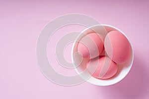 Three pink eggs inside the white bowl over pink background