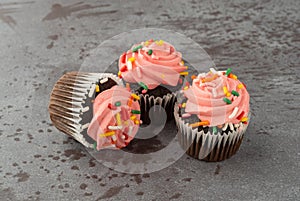 Three pink frosted chocolate cupcakes on a gray background side view