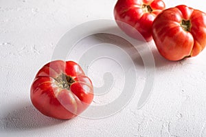 Three pink heirloom tomato vegetables, fresh red ripe tomatoes, vegan food, white stone concrete background