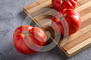Three pink heirloom tomato vegetables, fresh red ripe tomatoes on wooden cutting board, vegan food, stone concrete background