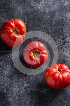 Three pink heirloom tomato vegetables in row, fresh red ripe tomatoes, vegan food, dark stone concrete background