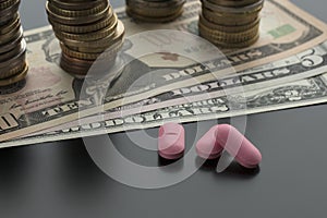 Three pink pills, tablets with dollar bills and stacks of coins
