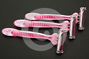 Three pink women`s razors on a black background