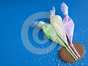 Three piping bags with colored icing for cookie decorating on the blue background