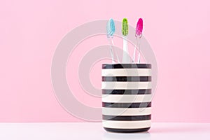 Three plastic colorful toothbrushes in glass on a pink background, close up