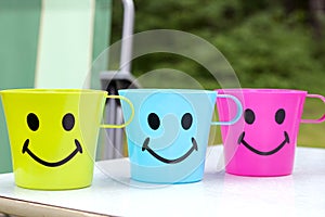 Three plastic cups with an attractive face with a smile are standing on a picnic table in nature