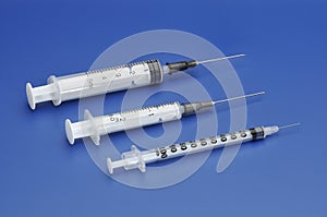 Three plastic disposable syringes with a needle on blue