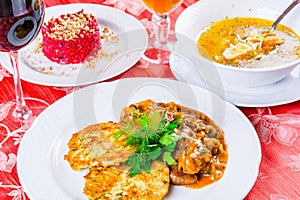 Three plates with lunch dishes on table. Salad with beets, vegetable soup and zucchini fritters