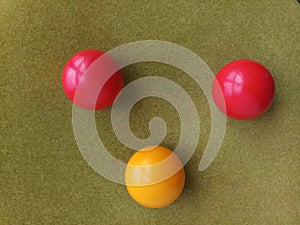 The three pool balls are in a three-pointed shape on a  green background. Two red pool balls and one yellow ball.