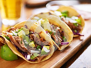 three pork carnitas street tacos in yellow corn tortilla with avocado, onion, cilantro and cabbage photo