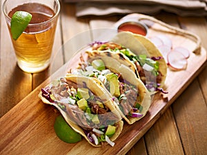 three pork carnitas street tacos in yellow corn tortilla with avocado, onion, cilantro and cabbage photo