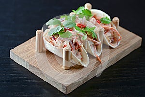 Three pork carnitas street tacos in yellow tortilla with onion, meat, cabbage and parsley on wooden board