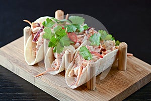 Three pork carnitas street tacos in yellow tortilla with onion, meat, cabbage and parsley on wooden board