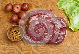 Three pound, raw, corn beef brisket, six small, red, potatoes and a leaf of cabbage, on a bamboo, wood, cutting board