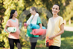 Three pregnant girls came to the park on fitness. A girl in a yellow T-shirt posing with a rug for yoga and a rope