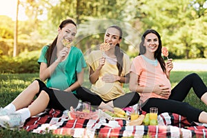 Three pregnant women posing in a picnic park with large colored candies