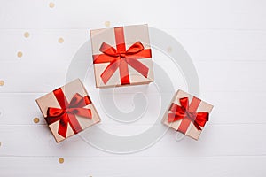 Three present boxes with red bow on wooden background.