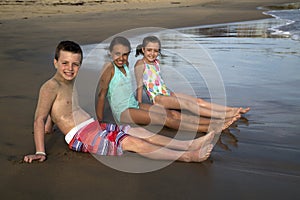 Three preteen children sitting on the beach in the water smiling